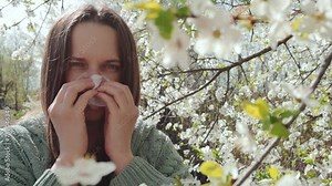 Pollen allergy. Sick ill young adult pretty woman sneezing in front of flowering cherry tree unhealthy female suffering allergic rhinitis using handkerchief vídeo de Stock