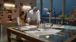 Wide angle shot of professional Asian painter teaching female student how to draw picture while giving class in art school in evening