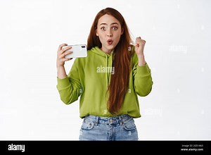 Excited teen redhead girl winning on mobile phone game, watching video on smartphone and celebrating, make fist pump and triumphing, white background Stock Photo - Alamy