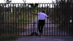 Plump blonde with short curly hair walks along asphalt road to metal...