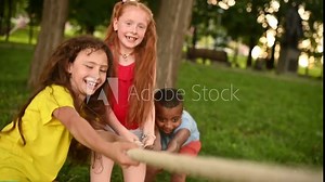 a group of children compete in a tug of war in the open air against the background of grass and park.