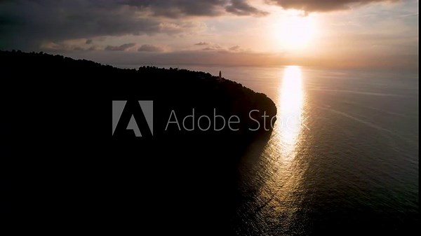 4K Aerial Drone video of popular summer destination, sunset over the cliffs with a lighthouse and a huge port of boats anchored at golden hour with seagulls flying. Port de Soller, Mallorca