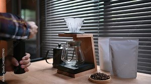 Close up hand crank coffee grinder by spilling hot water through a layer of ground on the filter. Trendy drink brewed coffee dripping into a glass pot with blank coffee packaging for mockup.