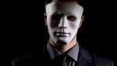 Anonymous suit man in mask folding hands on black background, illegal...