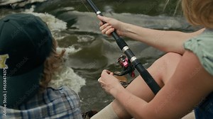 Unrecognizable woman holding spinning rod and spooling line onto reel while she fishing with her son