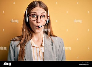 Young redhead call center agent woman overworked wearing glasses using headset afraid and shocked with surprise expression, fear and excited face Stock Photo - Alamy