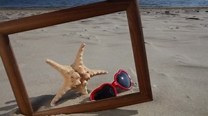 Marco de madera borde espacio de copia en blanco con concha marina y gafas de sol en la playa de arena