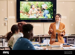 Waist up portrait of adult woman as female professor giving lecture to diverse group of students with educational video on screen Stock Photo - Alamy