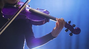 Close-up of young female musician playing violin on stage and her violin. Close-up of woman playing violin on opera stage or music hall.