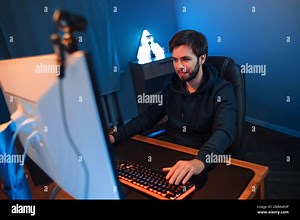 Young handsome pro gamer playing video games online on computer in darkroom, using webcam for live stream, recording vlog. Cyber sportsman participates in tournament with his team. Modern technology Stock Photo - Alamy