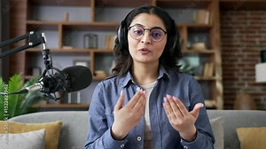 Webcam view. Young woman recording podcast looking at camera using microphone in home office. Female vlogger influencer conducts online broadcast, interview or webinar, speaks remotely via video call