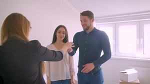 Female real-estate agent giving the keys from new home to happy young excited couple and shakes hands with them.