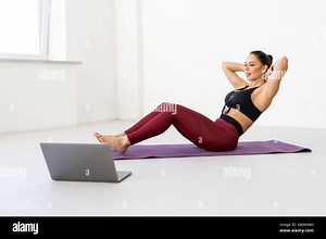 Positive young athlete exercising abs at home watching video workout lesson on laptop computer. Happy woman doing crunches following instructions of a Stock Photo - Alamy