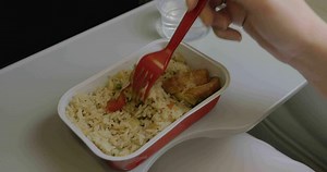 Close up clip of woman eating airplane dinner rise with vegetables by plastic fork against window