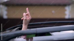 The car hatch opens and a female driver hand with a middle finger sticks out. A woman shows an abusive gesture to another driver. Rudeness on the road.