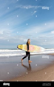 Full body side view of sportive female surfer in black wetsuit walking on wet shore near waving sea during training Stock Photo - Alamy