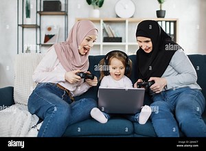 Old muslim granny, young mom in hijab and little cute girl with headphone playing video games at home, sitting on sofa with laptop and using joysticks Stock Photo - Alamy