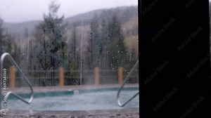View from the Window of a Luxury Hotel to Empty Swimming Pool in Rainy Weather. Blur. View from steamy panoramic windows onto a boiling hot tub. View of forest, mountains. Evaporation of water, rain.