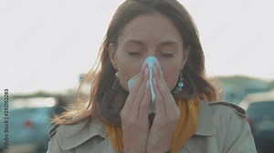 Face young woman stand coughs feel sick sneeze holds a handkerchief at outdoor fever cold allergy female nose sneeze lady runny tissue air pollution adult illness district slow motion