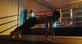 Young woman performing a plank exercise in a boxing gym with colored...