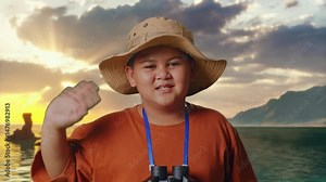 Asian Boy With Hat And Binoculars Using Magnifying Glass, Smiling And Waving Hand on Beach. Boy Researcher Examines Something, Travel Adventure, Close Up