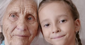 Affectionate happy old adult woman grandmother and cute adorable small kid granddaughter. Look at camera bonding laughing showing family love concept. Closeup portrait.