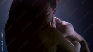 A woman and a man underwater, lovers deep inside on a dark background. There's light all around them. They are full of passion, hugging and kissing.