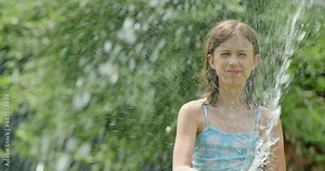 A joyful girl laughing while playing with a garden hose, refreshing herself on a hot summer day.