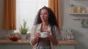 Dreaming Hispanic Caucasian woman Latina girl female housewife homeowner at kitchen rental own home morning drinking tea coffee aroma herbal drink healthy holding cup smile looking at camera wink eye