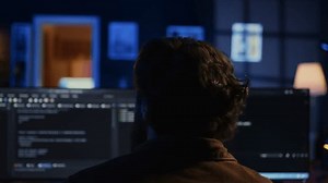 Software engineer writes binary code scripts on computer and drinks coffee. IT specialist in home office enjoying hot beverage while using programming to safeguard consumer data, camera B