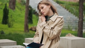 Free stock video - Caucasian female student talking on the phone with a notebook in the park.