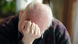 Distressed elderly man holding his fist to his forehead and shaking...