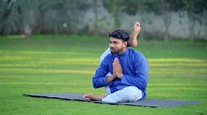 Indian man doing the Leg over Shoulder Yoga Pose or Eka Pada Sirshasana in a park