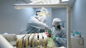 Oral surgeon, nurse doing medical operation on root canals in operating room. Dentist puts stitches on gum after surgery in the modern dental clinic. Dental surgery, installation of dental implants.