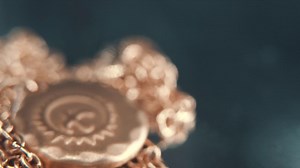 A detailed macro tilt down shot of a golden medallion necklace, flying bird in the middle of the sun symbol, on a rotating stand, mirror reflection, studio lighting, 4K video | Premium Stock Video Footage