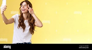 Positive charisamtic happy young girl curly-haired raise smartphone taking selfie show peace victory sign having video call stand yellow background Stock Photo - Alamy