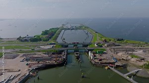 Aerial zoom in over the Afsluitdijk dam, revealing the Dutch water locks and flood control structures along the coastline.