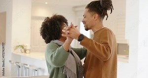 Diverse couple holding hands dancing in kitchen sharing moment with smartwatch and bar stools