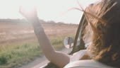 Carefree young woman driving convertible along sunny, rural field....
