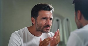 Un jeune homme souriant applique après le nettoyage de son visage une crème de jour ou de nuit pour prendre soin de la peau b