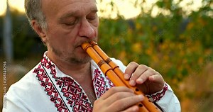 Large portrait of a male musician in a folk Ukrainian costume playing on a wooden pipe, pinching the holes on the pipe with his fingers. Folk folklore art. 4k, ProRes