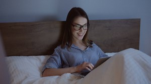 Smiling caucasian young woman in eyeglasses typing on the keyboard of the laptop late at night in the bed | Free Stock Video Footage