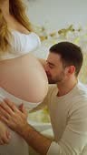 A close-up of a happy man kissing the bare belly of his pregnant wife.