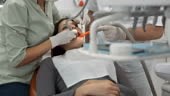 DOLLY shot of a female dentist drilling young woman's tooth while her...