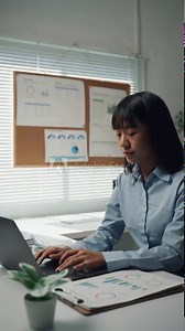 Unwell Asian office worker feeling sick, sneezing into a tissue while typing on her computer at her desk. Overworked and ill employee