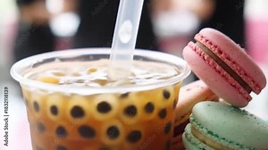 Close-up video of iced bubble tea with tapioca pearls in a transparent cup, accompanied by pastel-colored macarons. Suitable for concepts of trendy drinks, dessert pairing, café lifestyle, sweet treat Stock Video