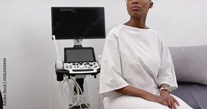 Woman in exam gown turning toward clinician on cue, adjusting eyeglasses and watching ultrasound