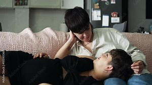 Lesbian expecting couple relax on a couch, caressing and sharing affection. The cozy indoor setting includes soft lighting and a comfortable atmosphere, highlighting their strong connection. Panning,