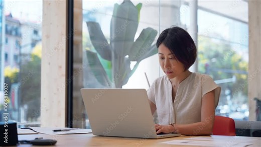 Focused mature eastern business woman working on laptop computer sitting at office workplace desk. Asian entrepreneur manager businesswoman finance analyst using pc for data analysing at workplace.