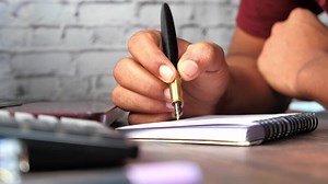 A man writing in a notebook with a pen on a desk